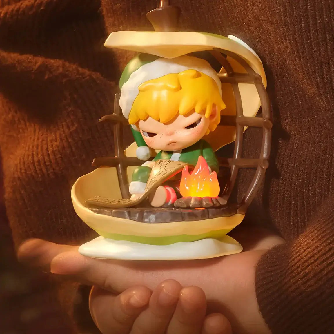 Figurine Labubu de la série "Apple Of My Eye" représentée en train de se réchauffer près d'un feu de camp.