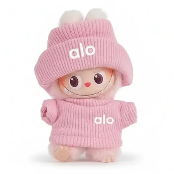 Poupée en peluche mignonne avec un chapeau et un pull rose, portant le logo 'alo'.