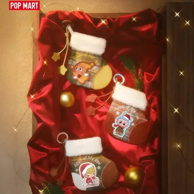 Chaussettes de Noël Labubu Apple Of My Eye décorées sur tissu rouge avec des ornements festifs.