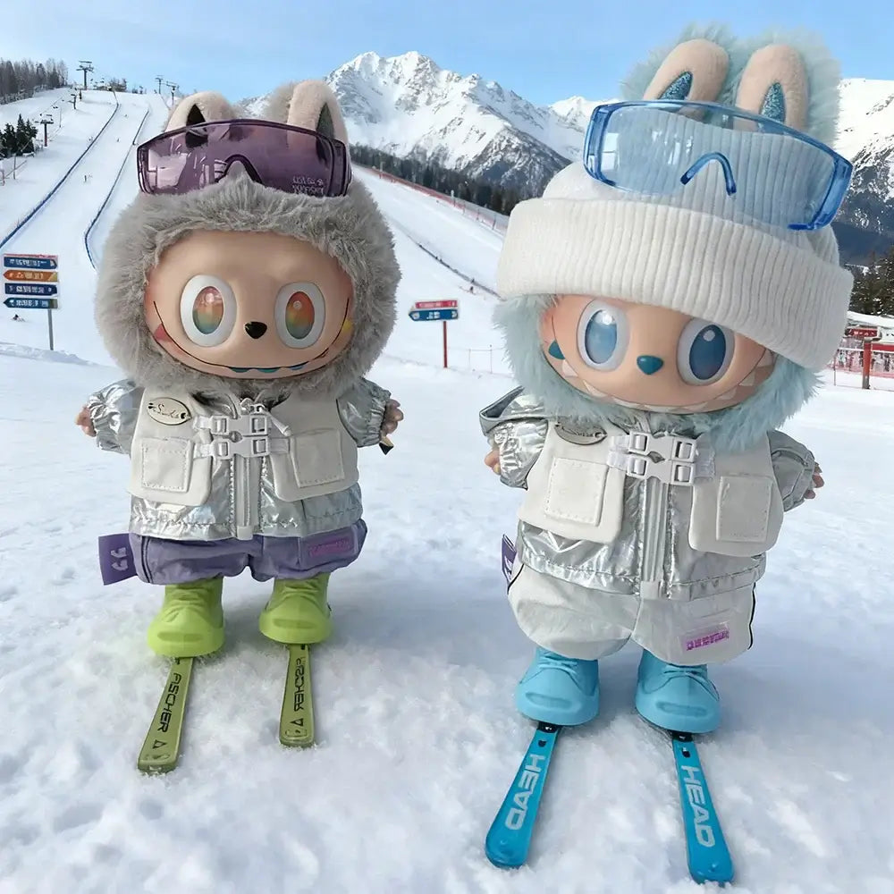 Deux personnages Labubu en tenue complète ski sur les pistes, avec skis, lunettes et paysage montagneux en arrière-plan.